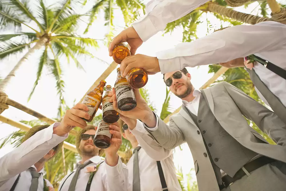 A groom and his groomsmen holding beers celebrating right after the wedding