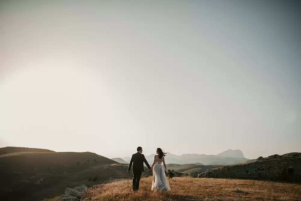 A bride and groom standing outside on a large hill.