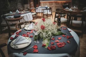 Romantic table setting with red rose petals, a floral centerpiece, and elegant dinnerware in an intimate wedding venue.
