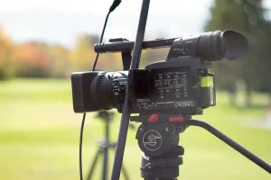A black camera on a tripod films on a green field