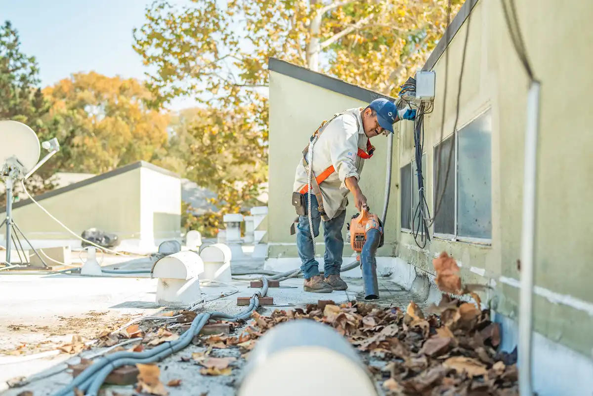 a commercial roofing contractor blowing leaves off a commercial roof